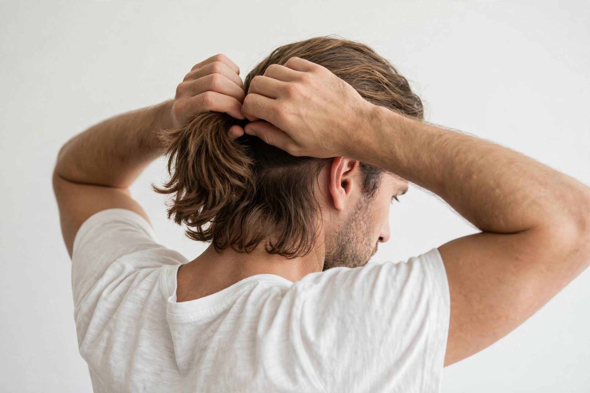 Man tying his lob into a low ponytail, hands gathering hair, lifestyle photography