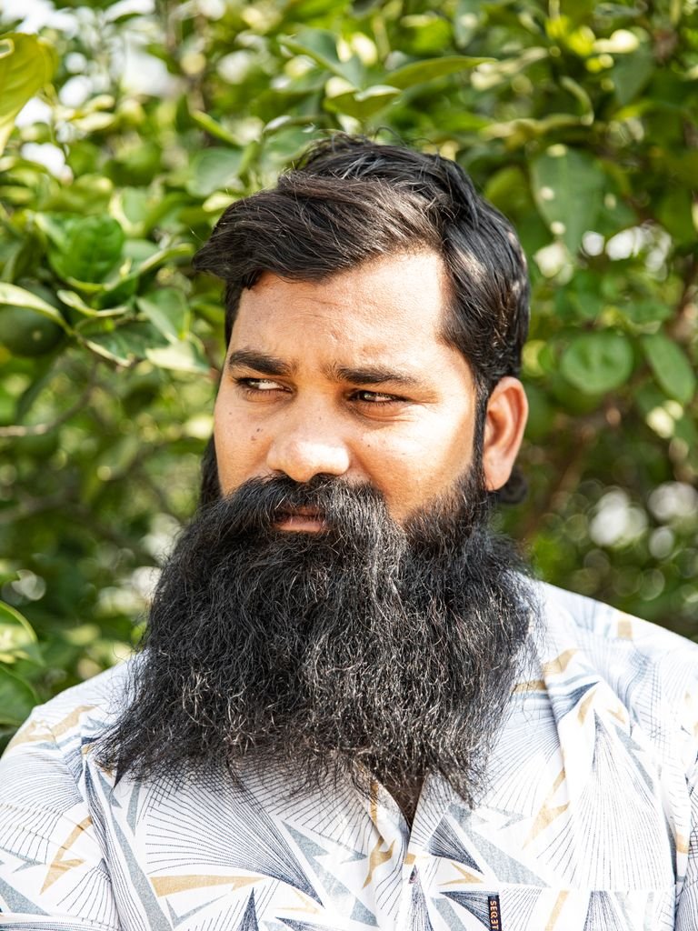 Stylish bearded man wearing a patterned shirt against a leafy green background outdoors.